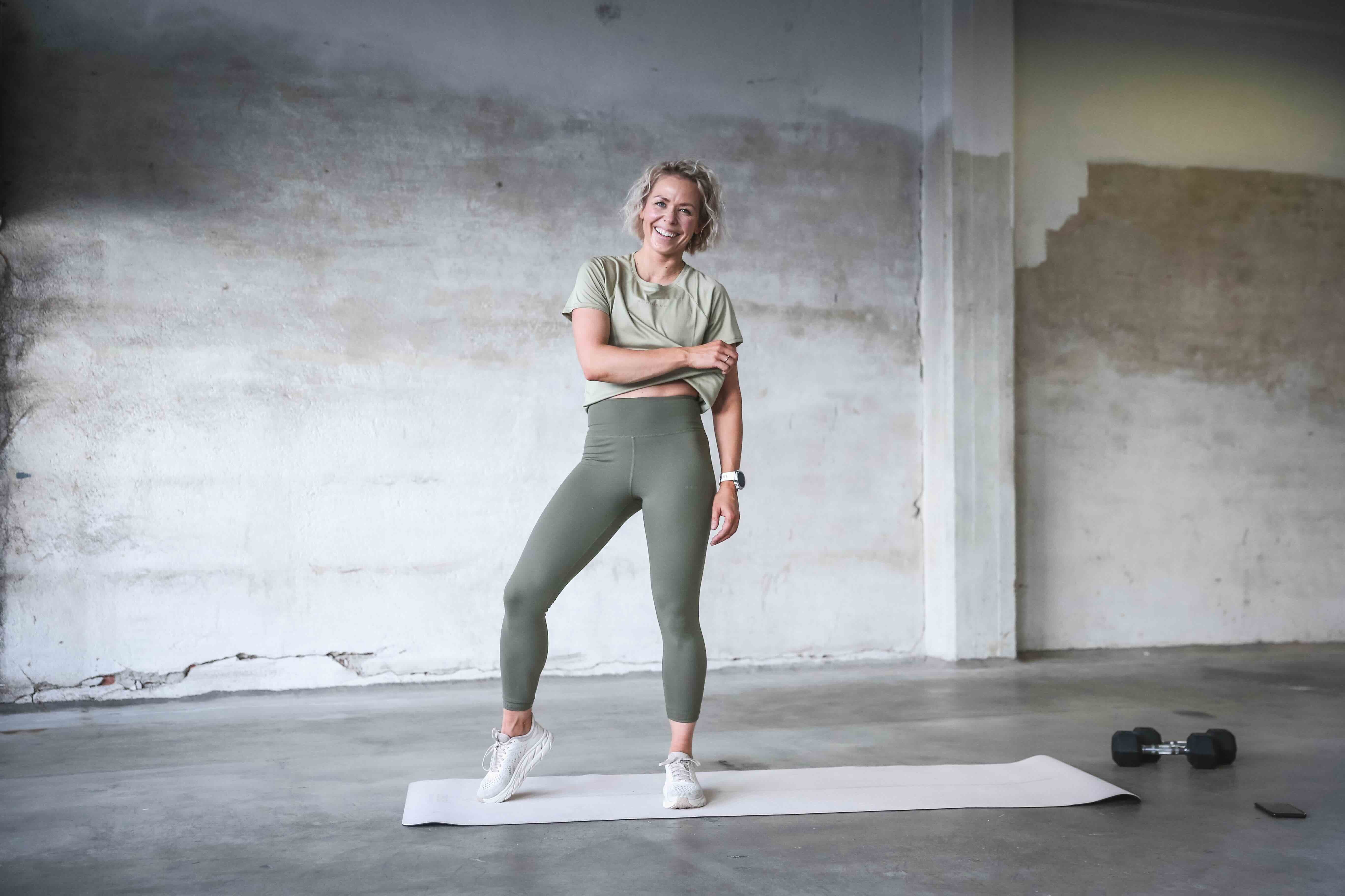 A person in workout clothing stretching on a yoga mat in a spacious, minimalist gym environment.