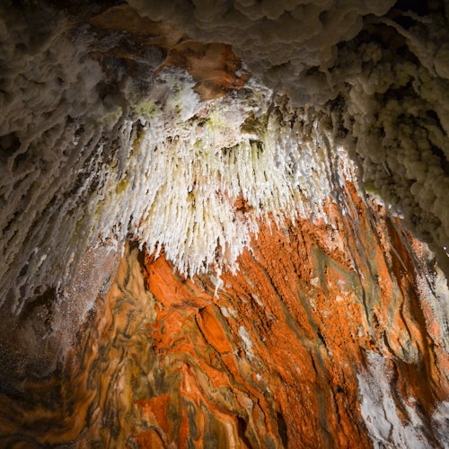 A cave ceiling with intricate white stalactites and vibrant orange and brown mineral formations.