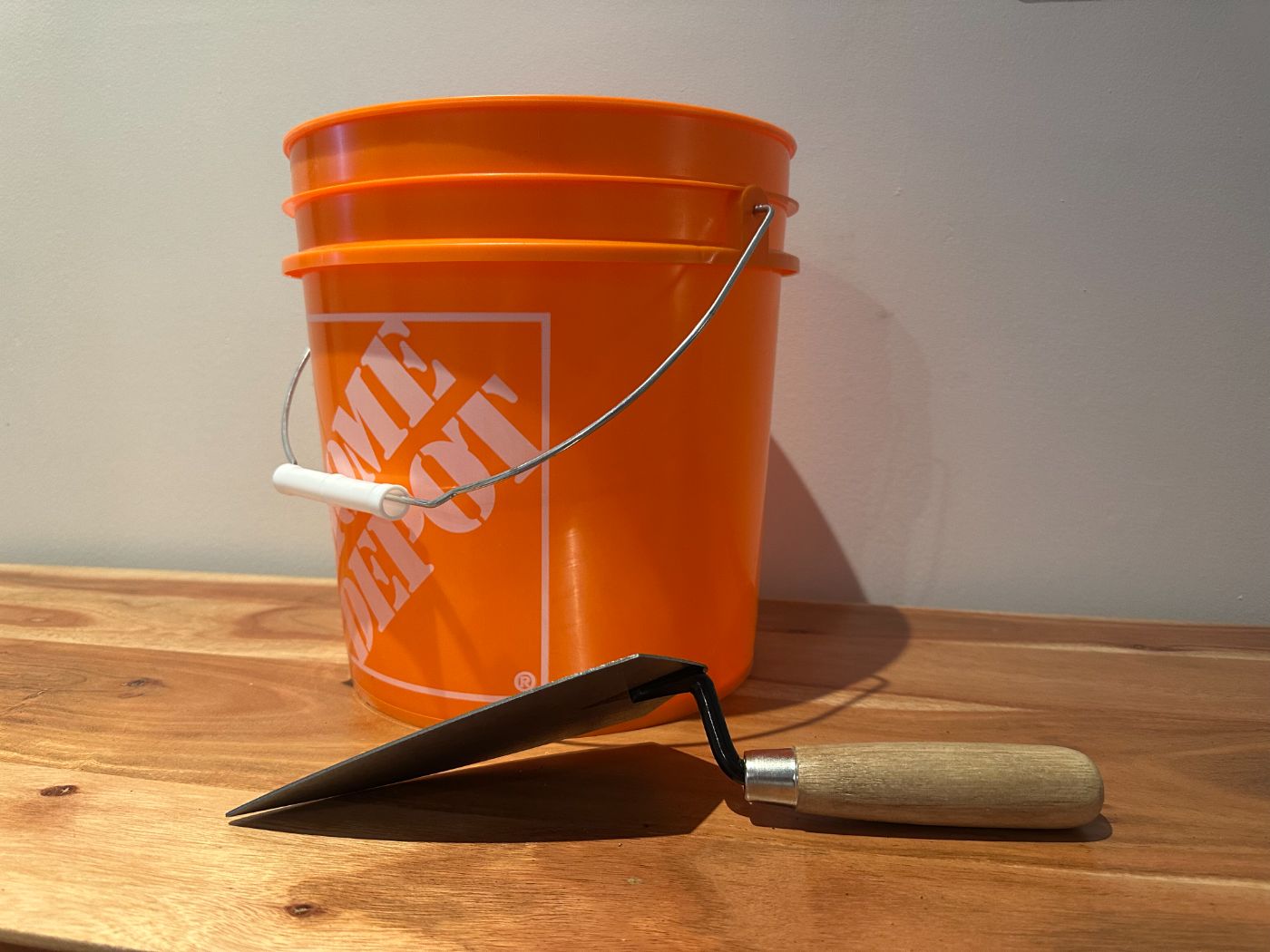 Seau orange Home Depot avec truelle à manche en bois posés sur une table en bois