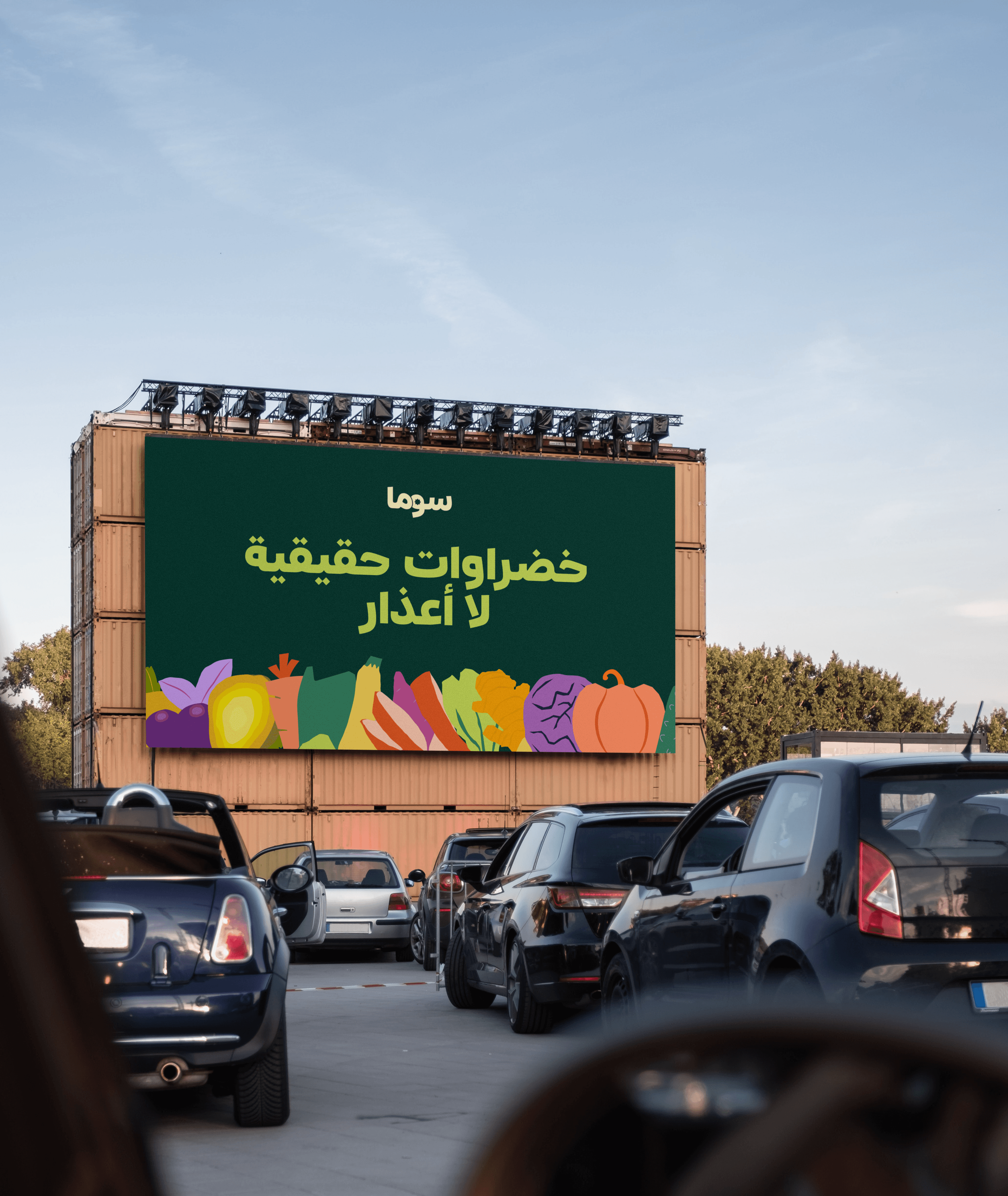 A large-scale OOH billboard mockup for SOMA displayed on a structure of stacked shipping containers in an urban environment. The design features the SOMA brand name and the tagline "real vegetables. no excuses." in Arabic script, using lime-green typography over a deep forest-green background with illustrative vegetable accents.