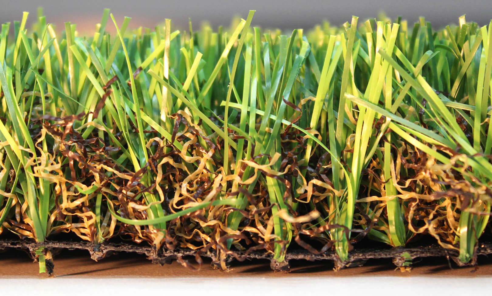 This close-up image shows the intricately orange, brown, and green artificial grass fibers within AGL Grass North's natural-looking Monte Carlo 60.
