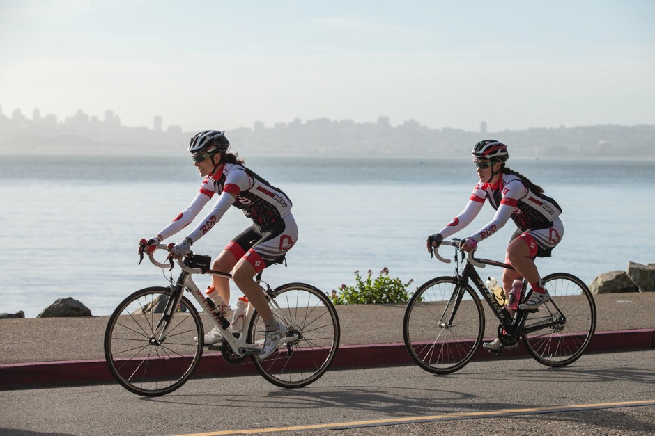 Two cyclists racing in front of a body of water.