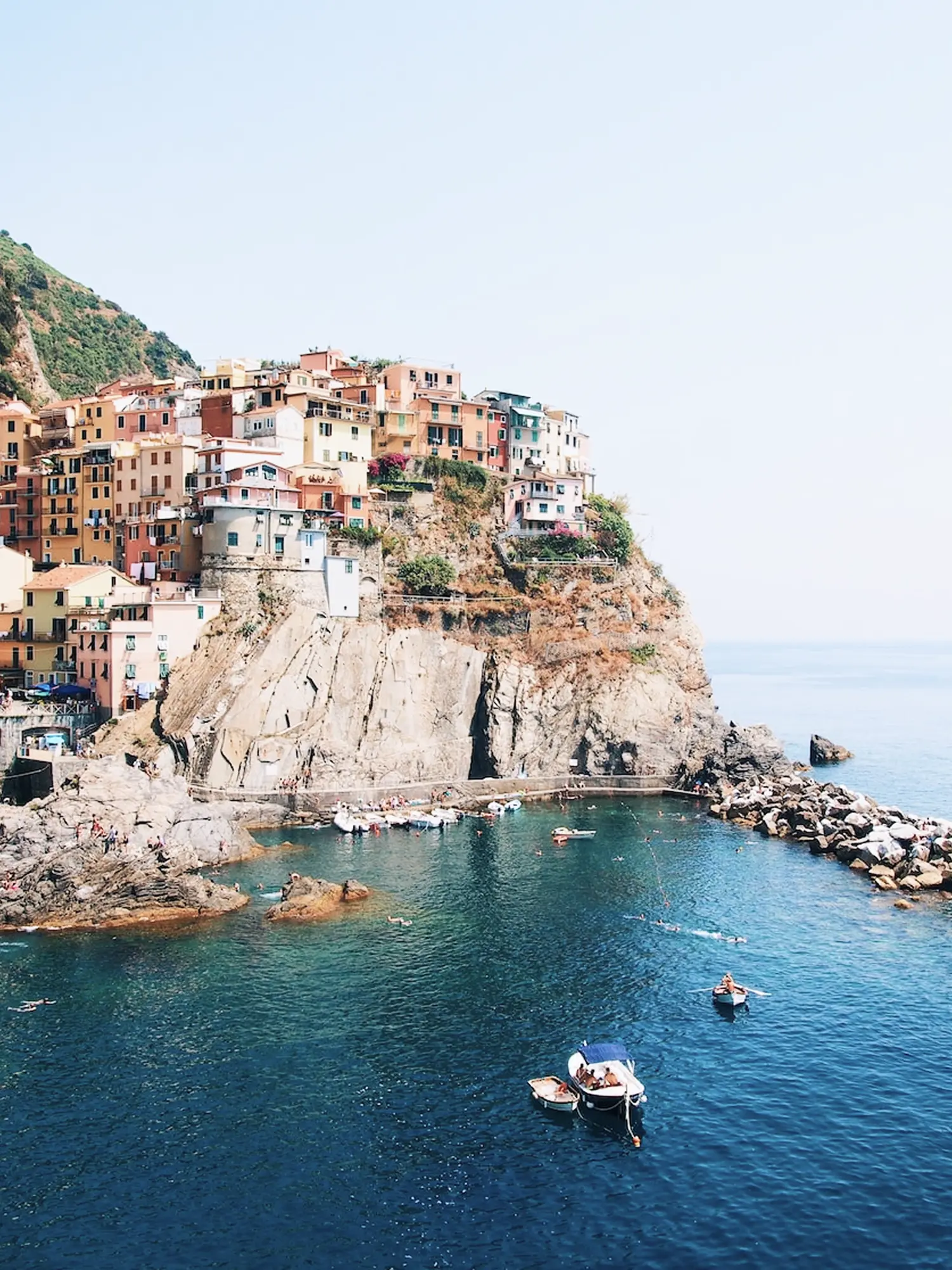 Luftige Aufnahme von Manarola in den Cinque Terre mit bunten Häusern auf der Klippe und Booten im Hafen.