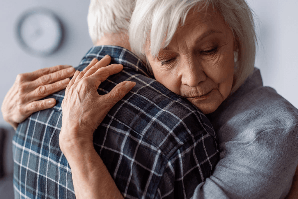 senior woman with closed eyes embracing husband sick on dementia