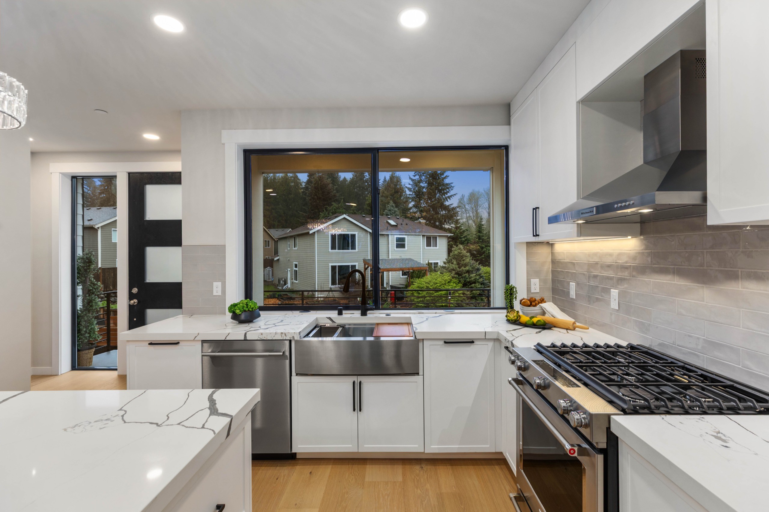 High-end chef's kitchen with white shaker cabinets, stainless steel farmhouse sink, professional gas range, wall-mounted range hood, and garden-view window