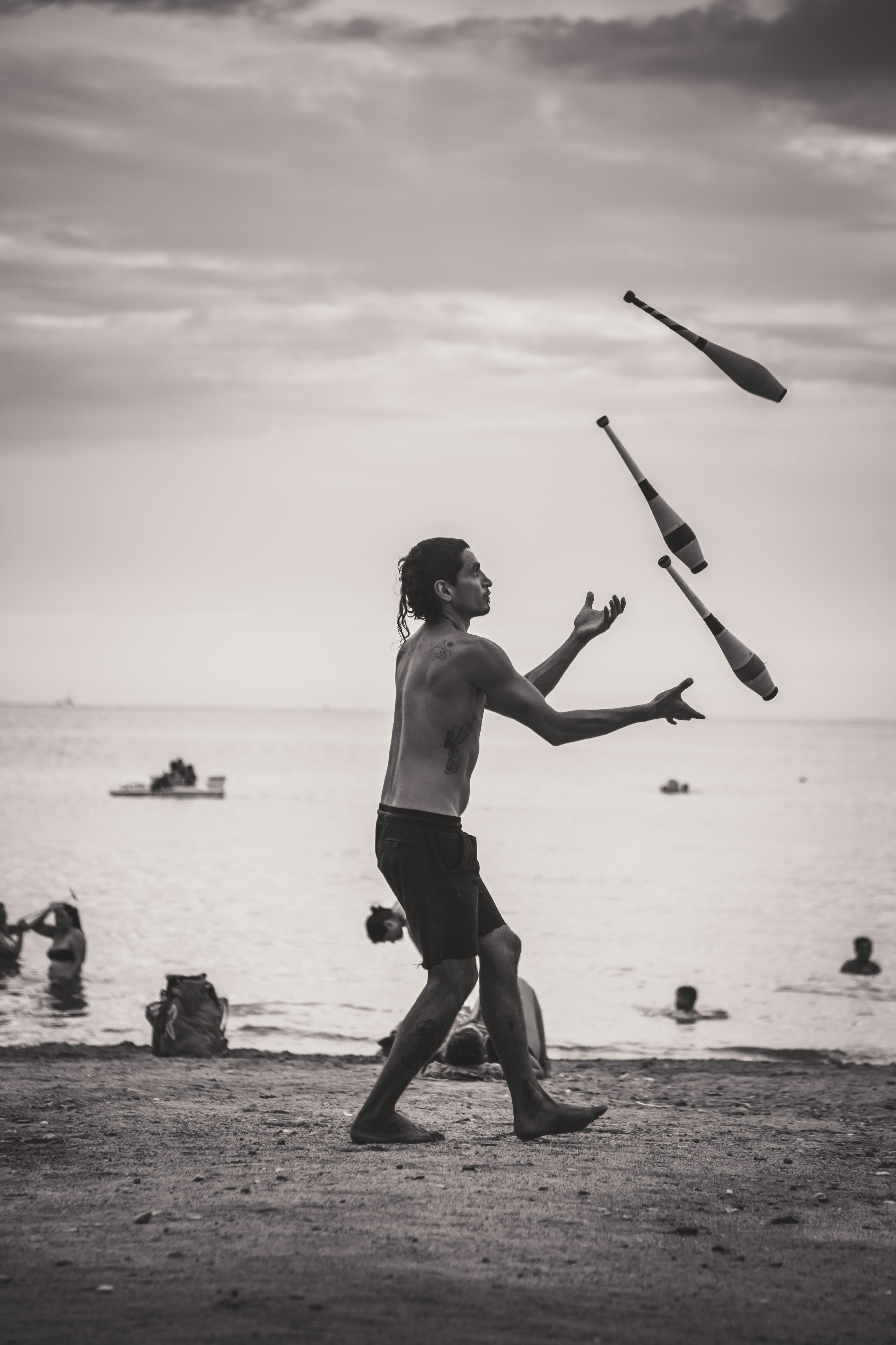 man juggling baseball bats on beach.