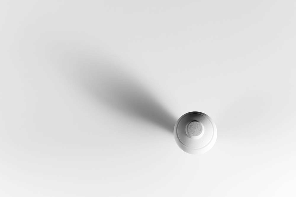 A wooden spinning top viewed from above, casting a long diagonal shadow across a clean, white surface.