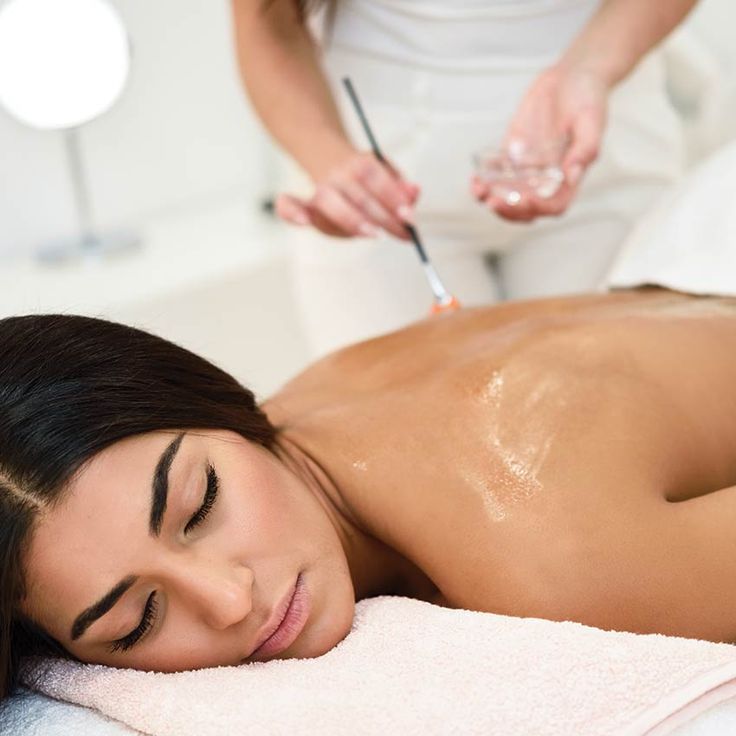 A woman lying down with a towel wrapped around her head, her face glowing with facial oil. She has a peaceful expression, enjoying a skincare treatment.