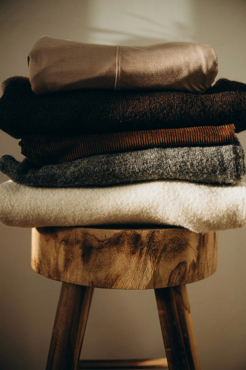 Close-up of stacked, folded organic fiber garments in neutral earth tones on a wooden surface