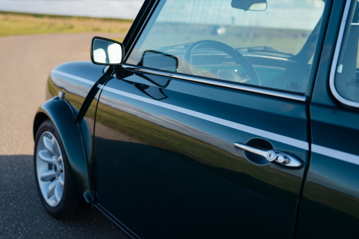 Close-up of a black car's side view mirror and sleek body, showcasing its shiny finish on a smooth road.