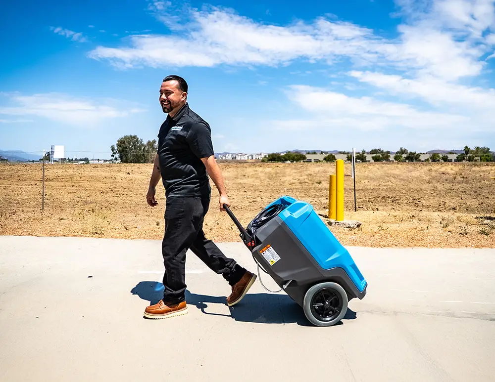 NewGen Restoration team member walking outdoors with a commercial dehumidifier, used for water damage restoration in San Diego.