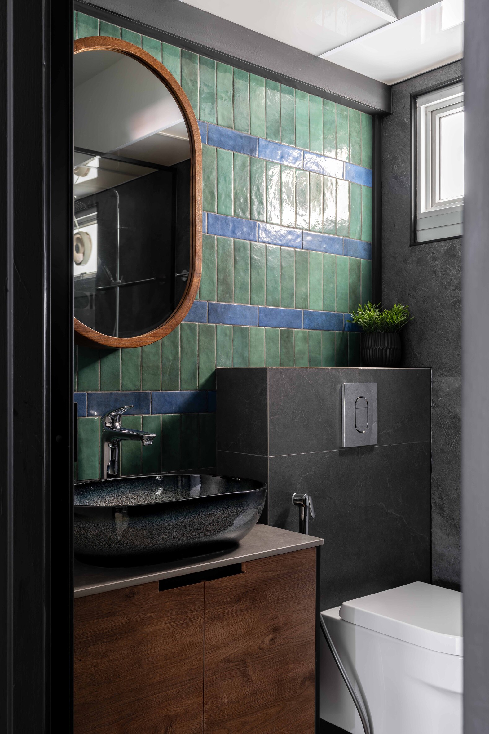 Modern bathroom featuring a large mirror, stylish sink, and textured green wall tiles. A wooden cabinet is visible.
