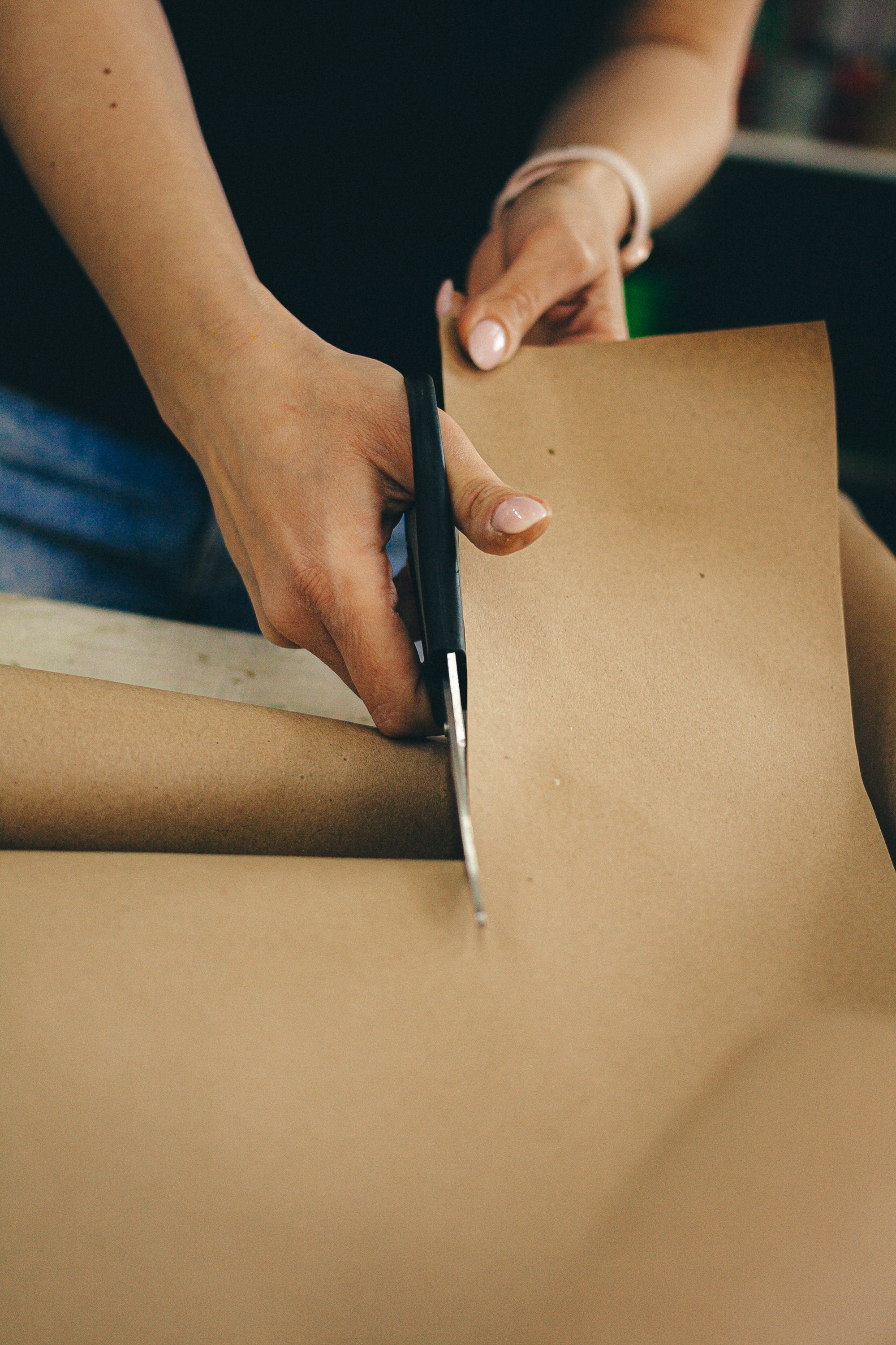 Hands cutting a sheet of kraft paper from a roll with black scissors