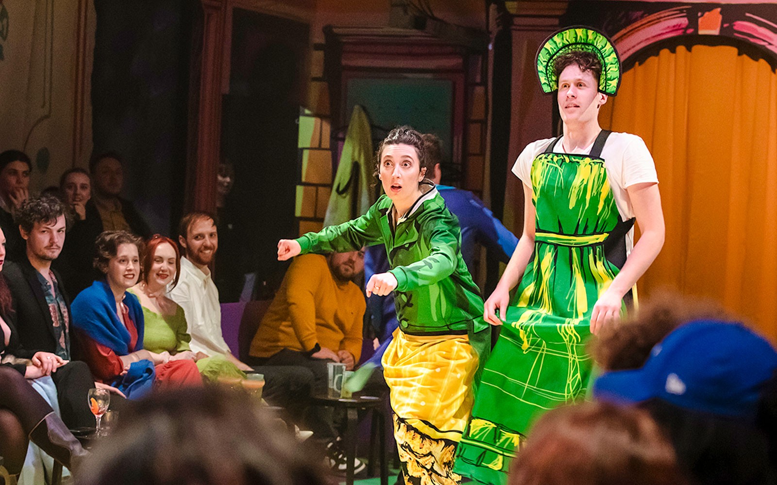 演员们穿着色彩斑斓的服装在舞台上表演《偏见与偏缘》，观众们正在观看。