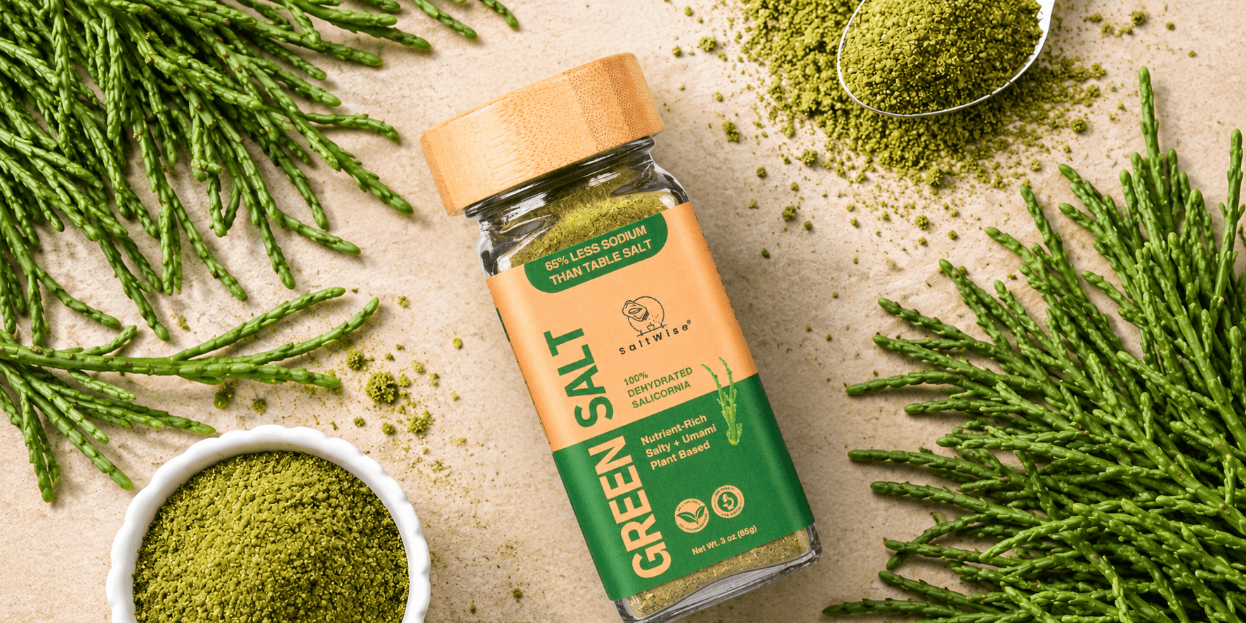 SaltWise Green Salt made from Salicornia, surrounded by fresh sea asparagus and green seasoning powder on a sandy background.