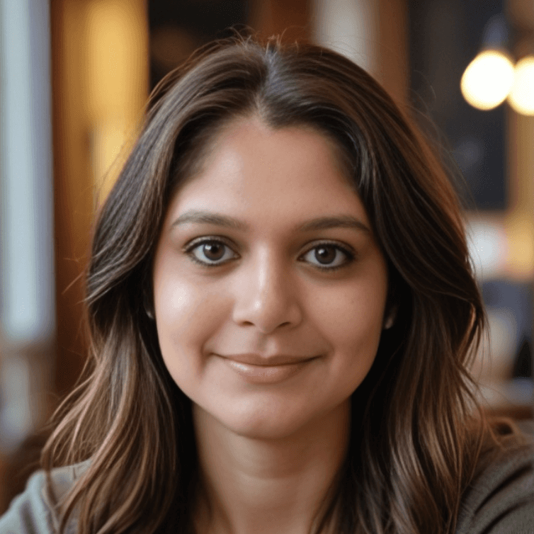 A person with long, dark hair smiles softly at the camera, exuding a sense of wellness. The background is blurred, featuring warm lighting and soft colors, suggesting a cozy indoor setting. She is nutritionist vasundhara agrawal.