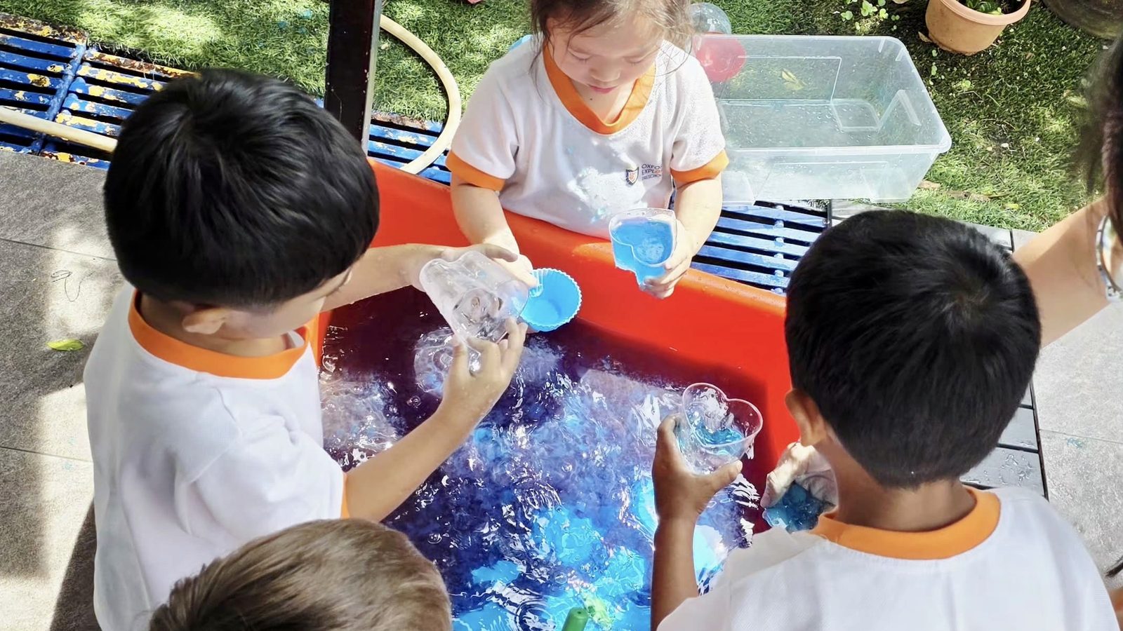 Preschool children at Oxford Explorers Singapore experimenting at an outdoor water tray.