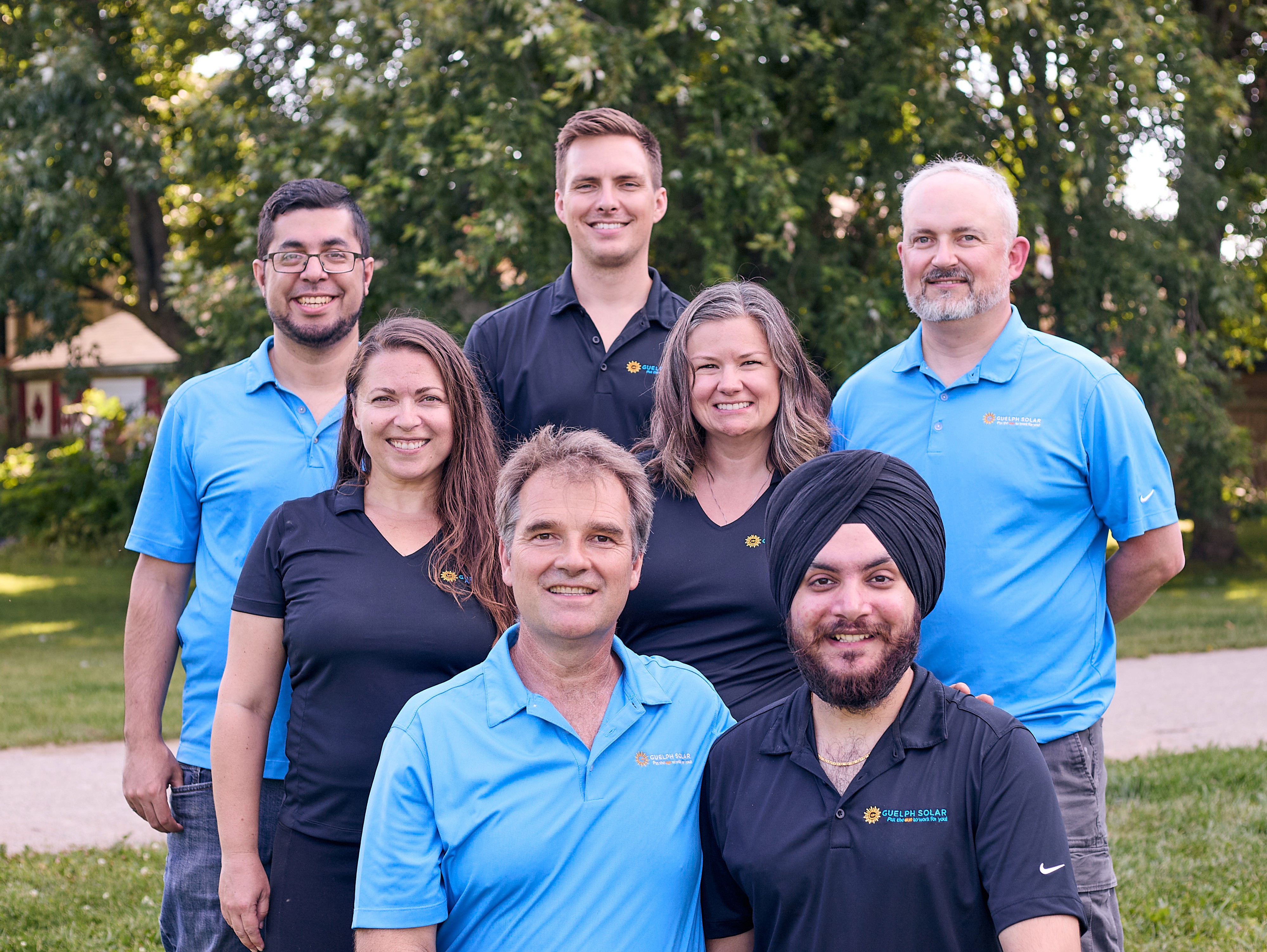 The Guelph Solar team, wearing matching blue shirts, posed together outdoors with trees in the background.