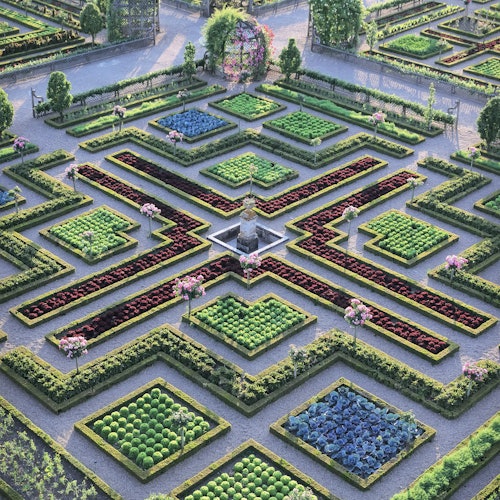 Συμμετρικός κήπος με τακτοποιημένες ανθοστήλες και περιποιημένους φράχτες, με κεντρικό σιντριβάνι και μονοπάτια που σχηματίζουν το σχήμα Χ.