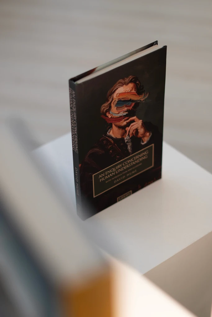 A woman with long hair and a black blazer holds a copy of Boethius's "The Consolation of Philosophy" next to her face, published by Logos.