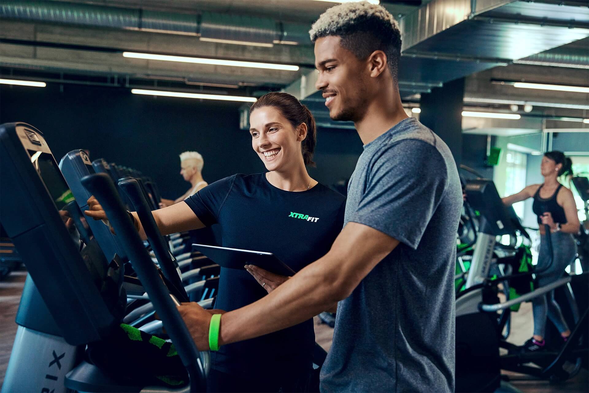 Ein Personal-Trainer von XTRAFIT hilf einem Sport-Einsteiger bei der Einstellung der Fitnessgeräte im XTRAFIT Fitnessstudio.