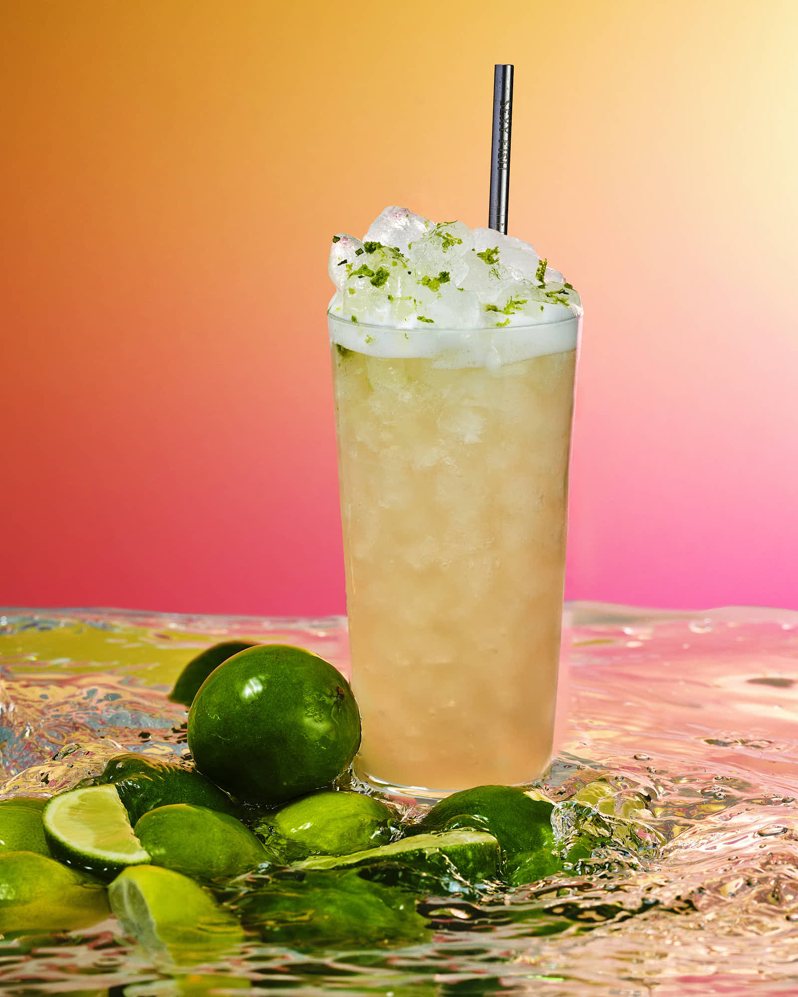 A refreshing drink in a tall glass, topped with whipped cream and a straw, surrounded by lime slices.