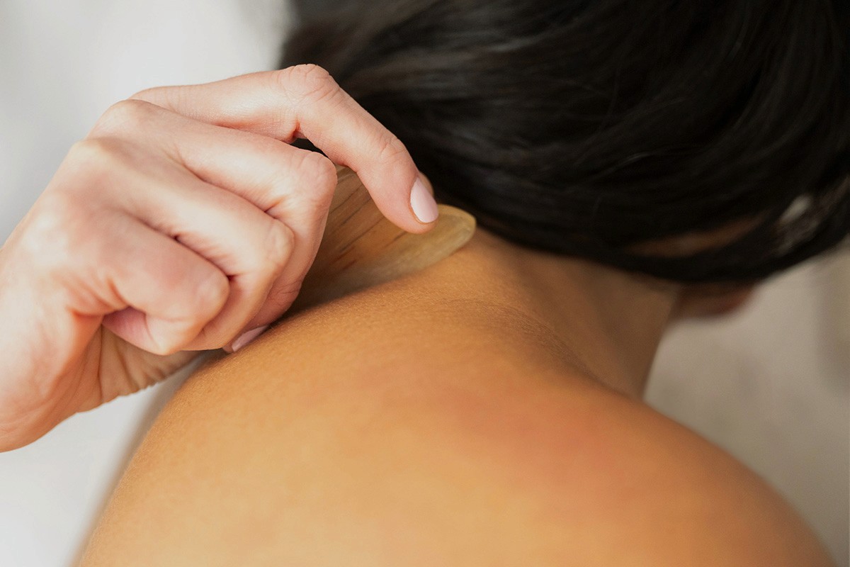 Ruth performing Gua Sha on a patient's neck with a smooth tool, using gentle downward strokes to relieve muscle tension.