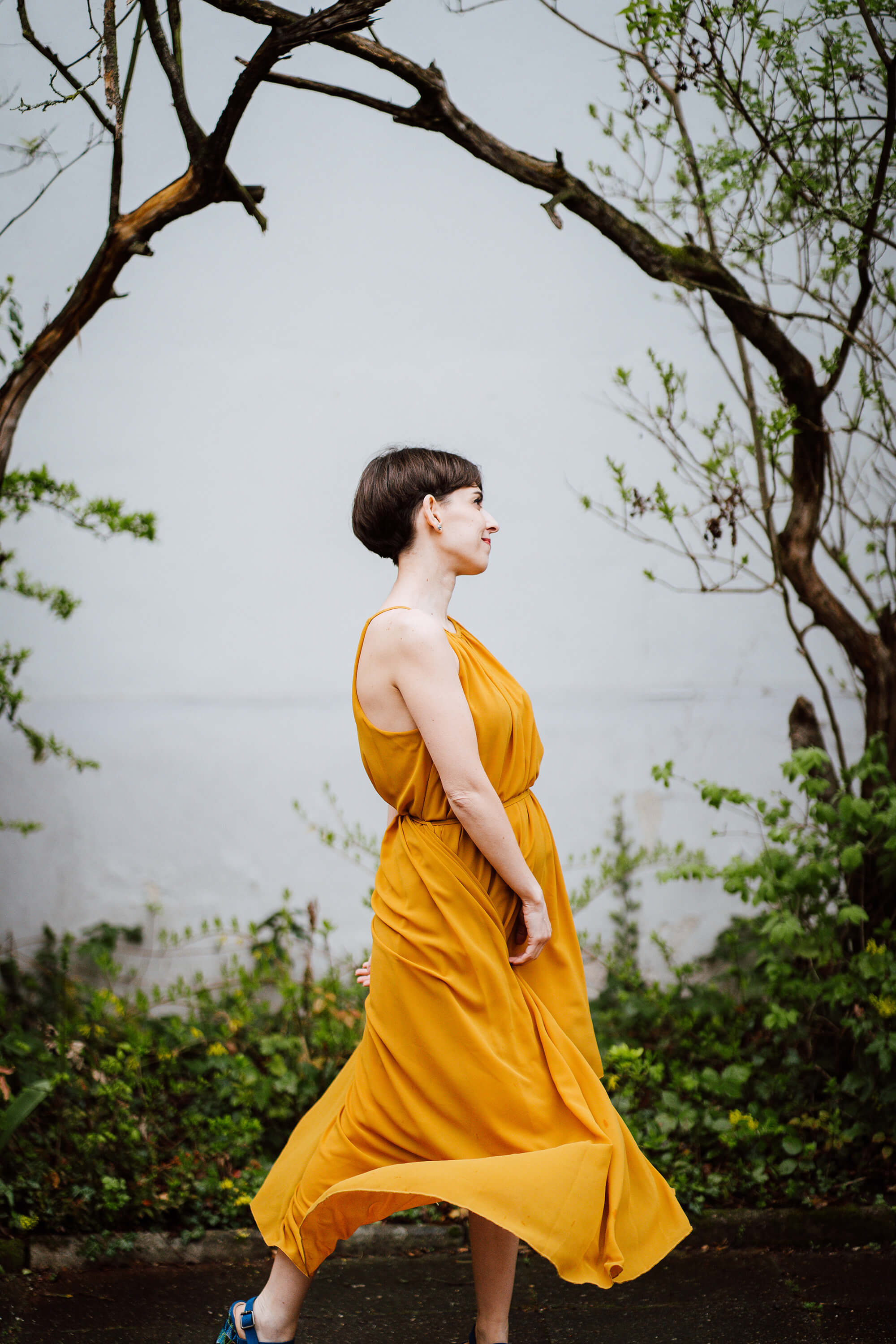 Francesca Introvaia in profile against a textured wall with spring branches overhead.
