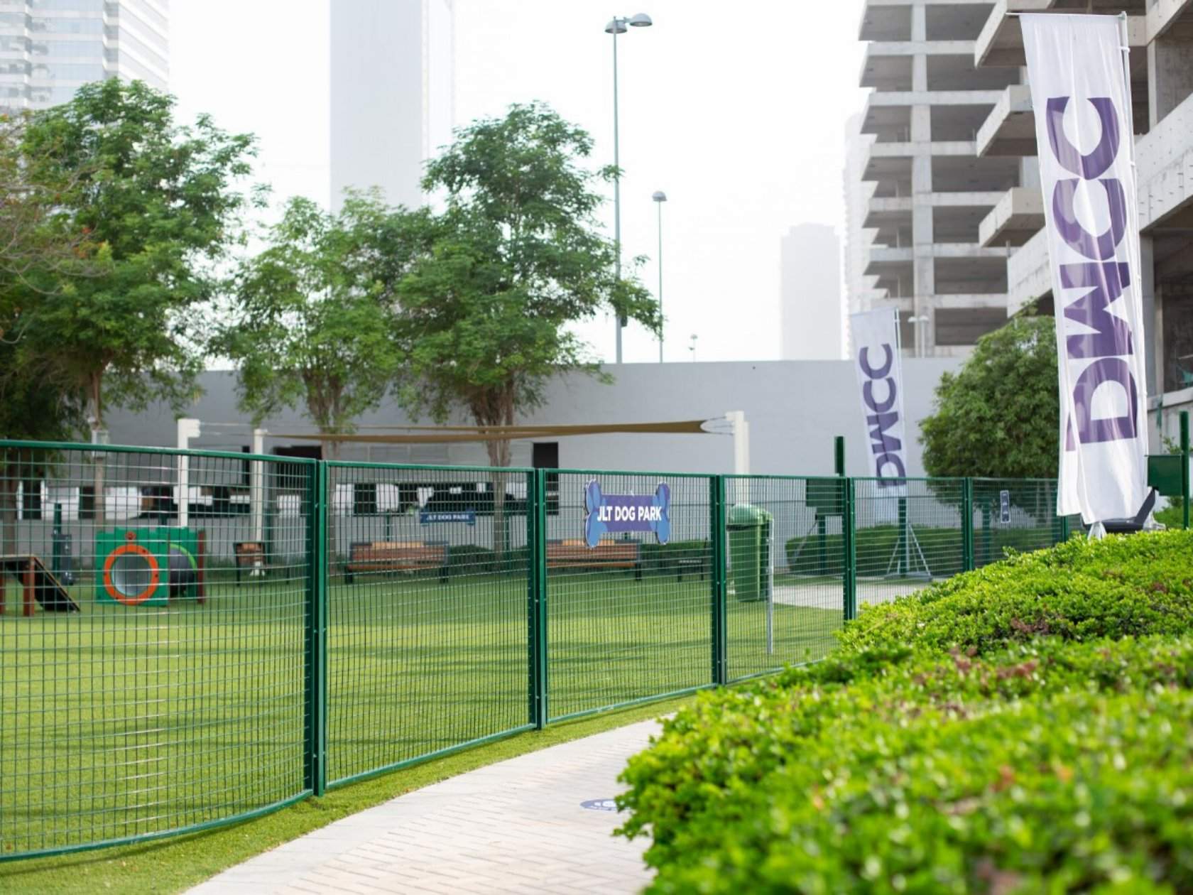 The JLT Dog Park with green fencing, agility training equipment, and greenery.