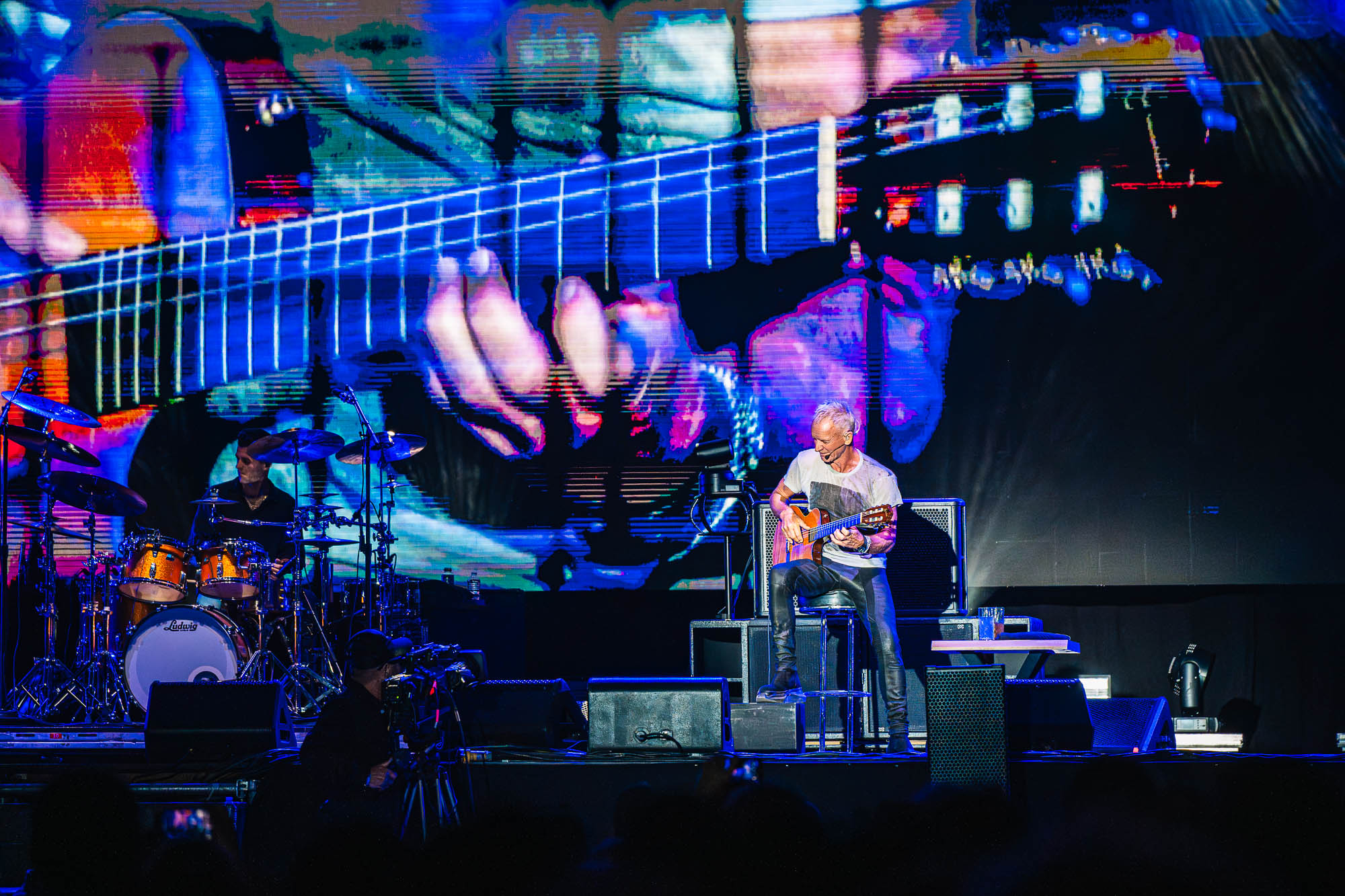 Guitariste assis en gros plan devant une projection vidéo de ses mains sur les cordes