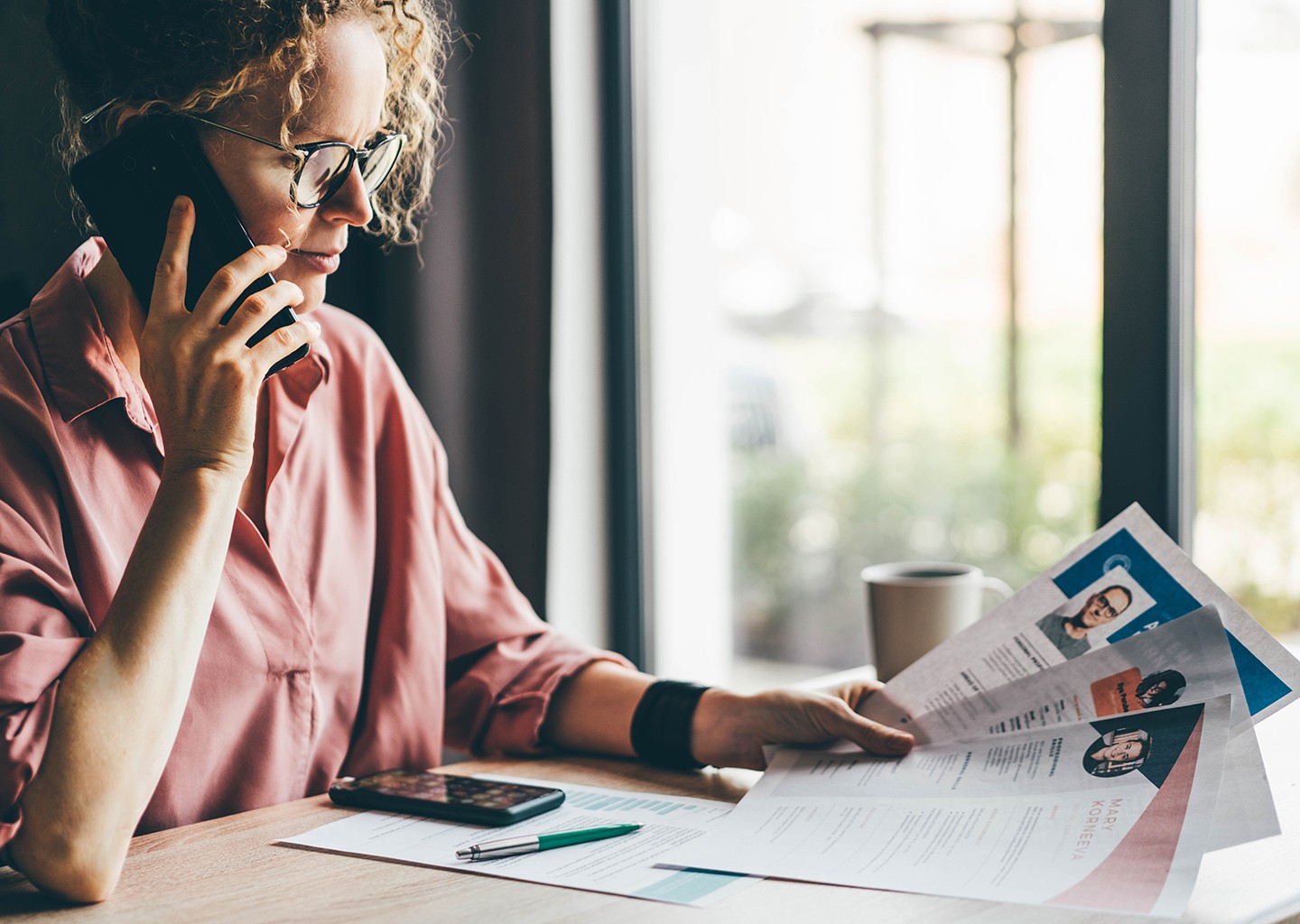 Recruiter sedua ad una scrivania con più curriculum davanti a simboleggiare esperienza vs. titoli di studio. Ambiente d’ufficio moderno con luce naturale.