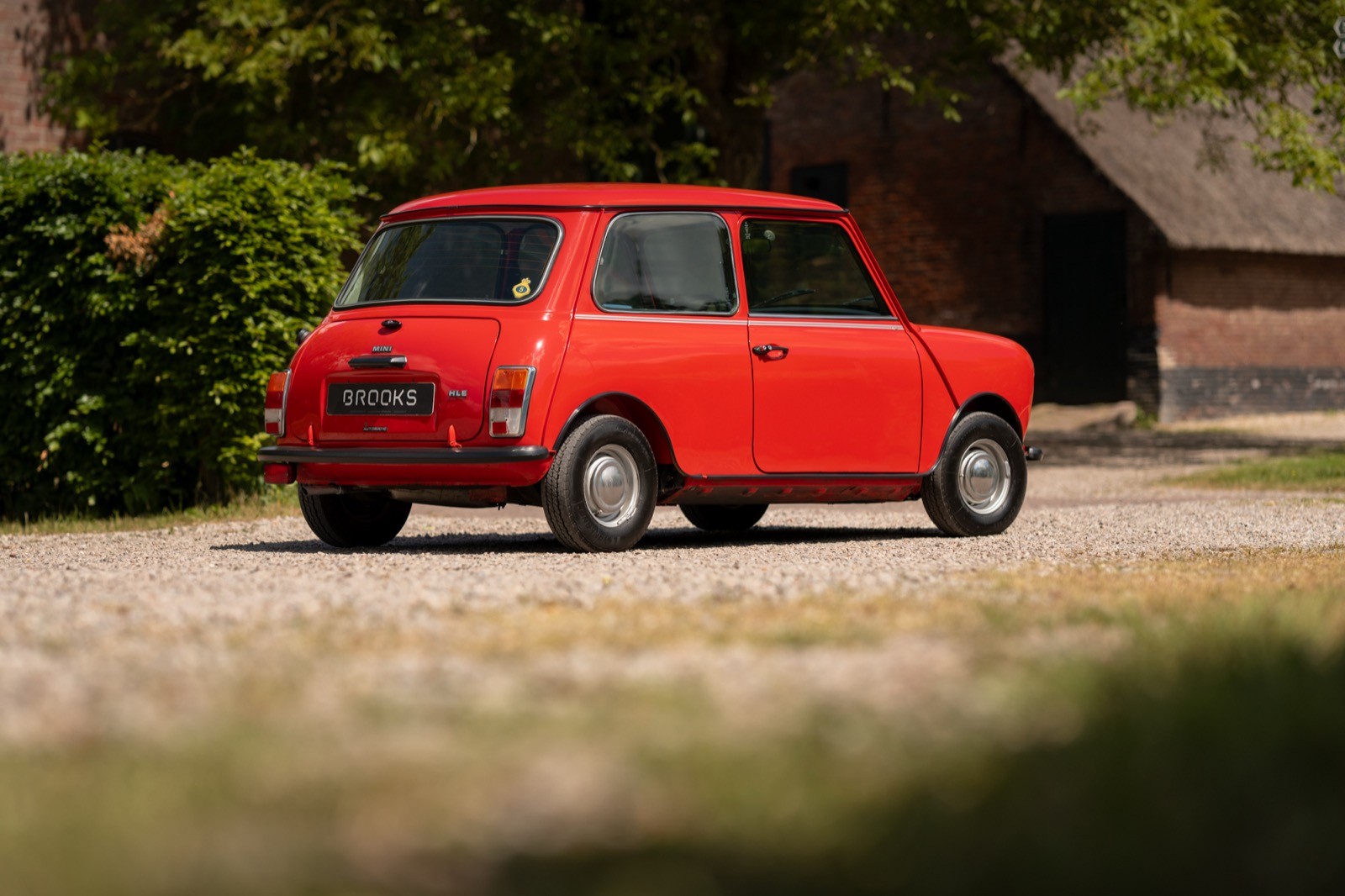 A bright red car parked on a gravel driveway, surrounded by greenery and a rustic building in the background.