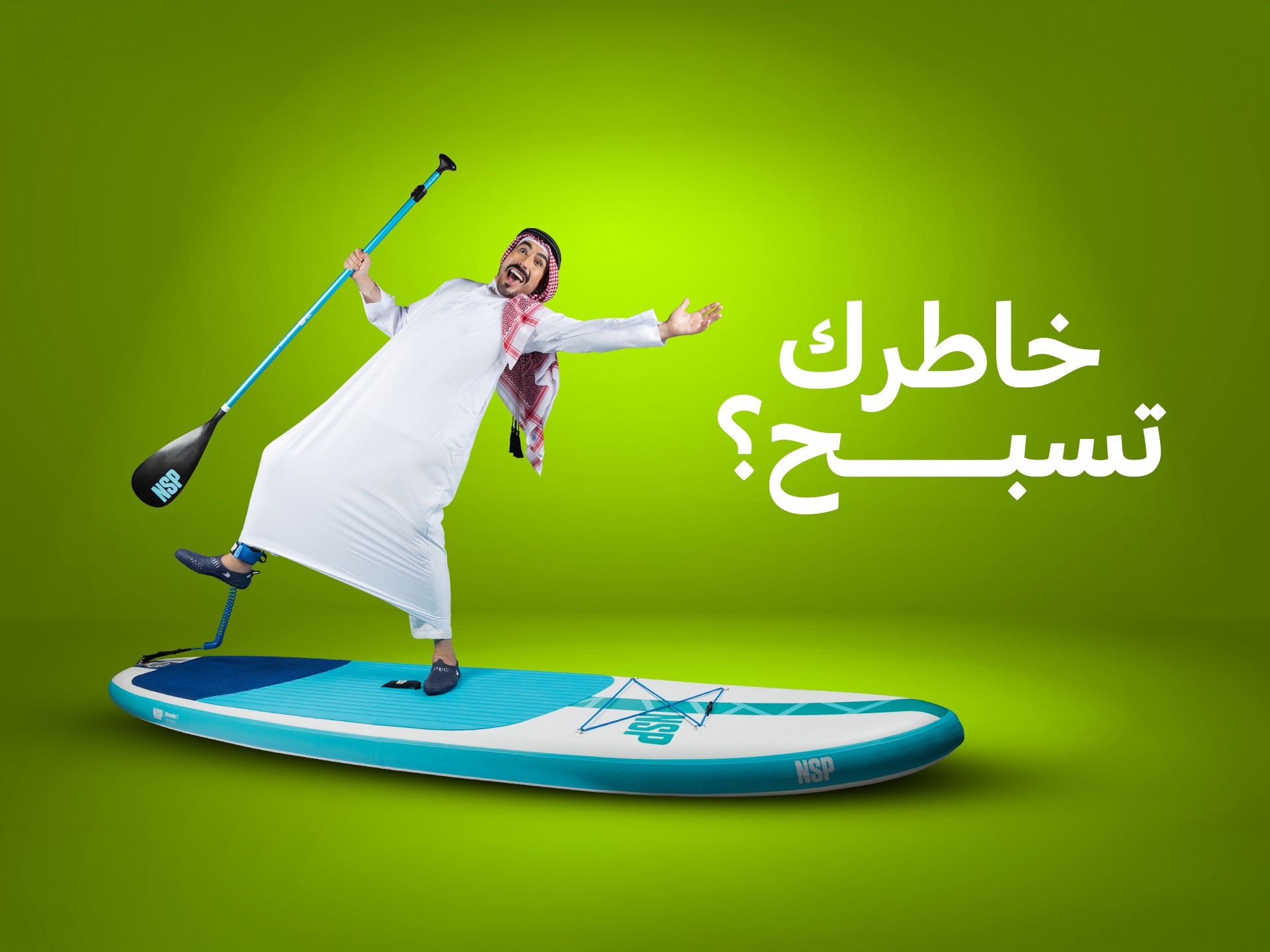 A man in traditional Qatari dress balancing on a paddleboard with a paddle, against a bright green background with Arabic type.