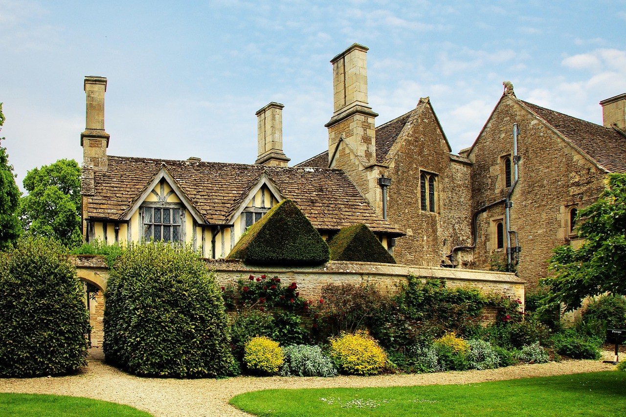 Historic stone manor with chimneys and gabled roofs, surrounded by lush gardens and topiary. A serene and tranquil English countryside scene.