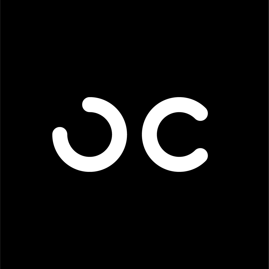 Person wearing a blue puffer jacket and red backpack standing in front of a light blue building on a city street.