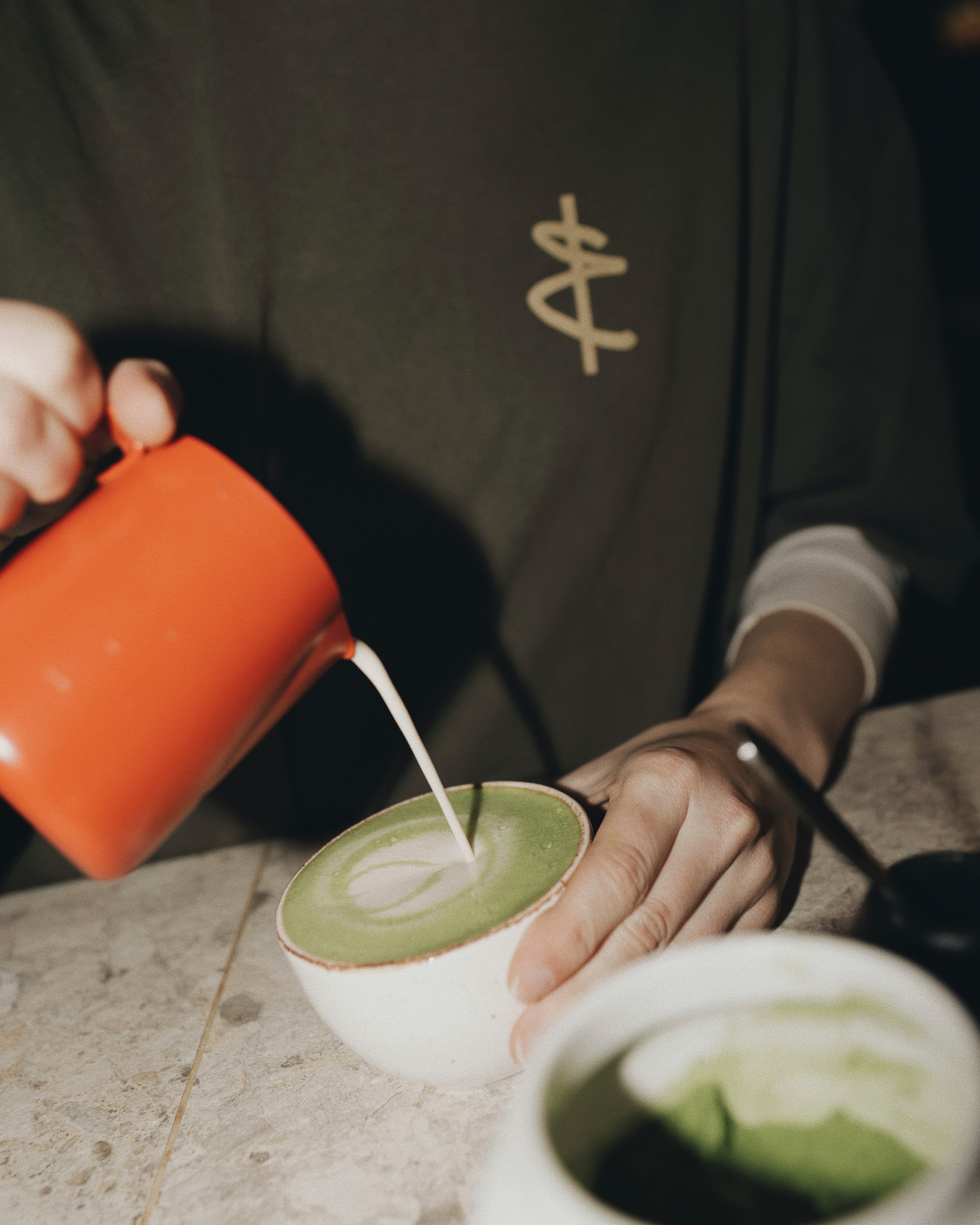 Barista pouring milk into a matcha latte to create latte art.