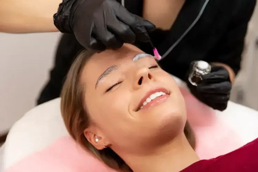Smiling client receiving numbing treatment for corrective eyebrow procedure in a professional studio.