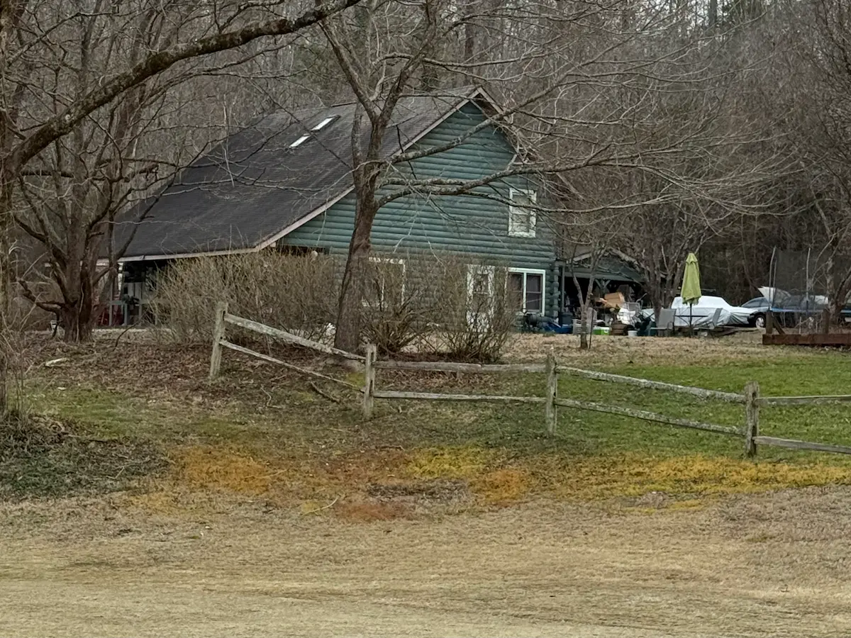 A quiet rural house surrounded by bare trees, viewed from a distance