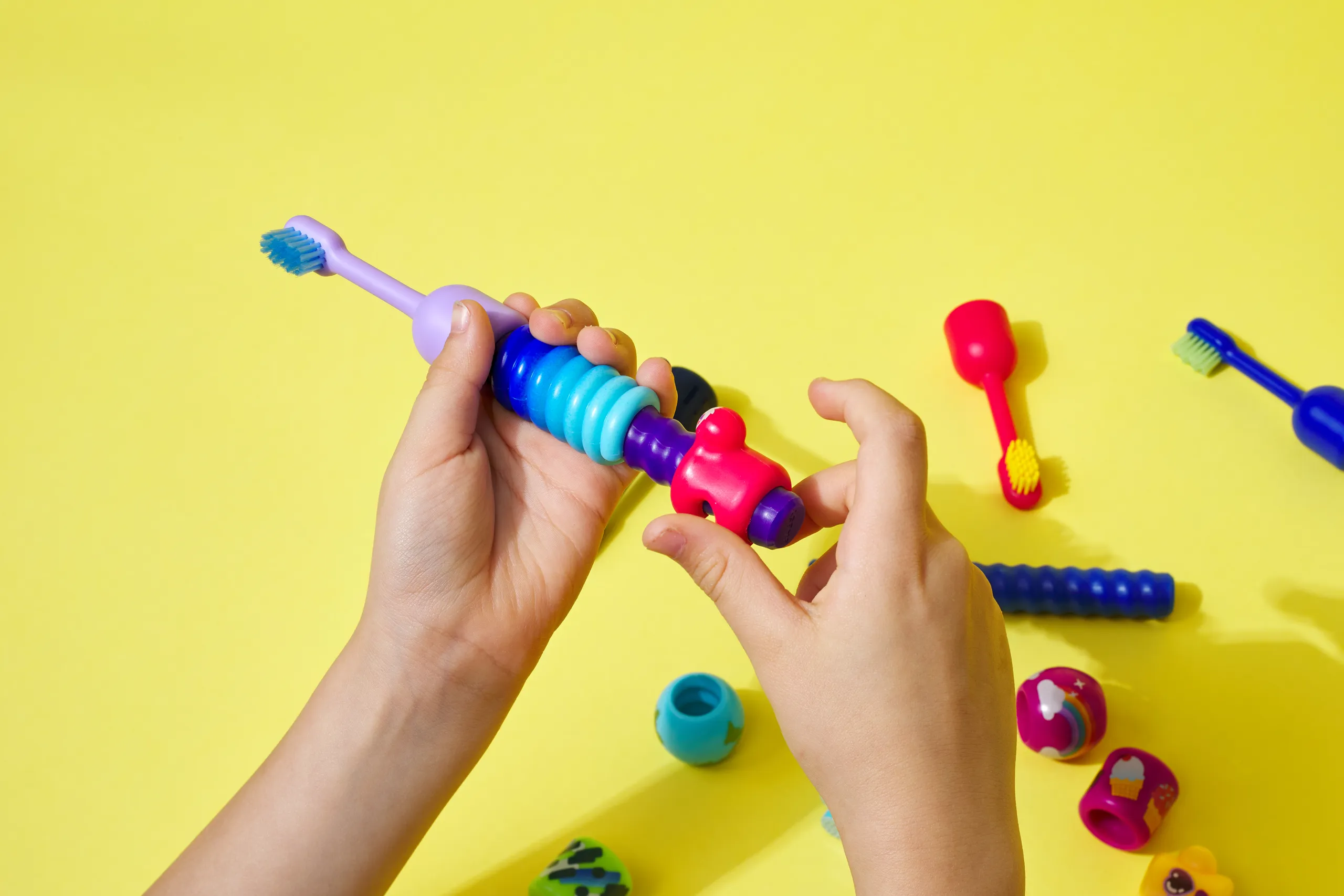 Child’s hands assembling colorful pieces onto a BABSY Build-A-Brush toothbrush