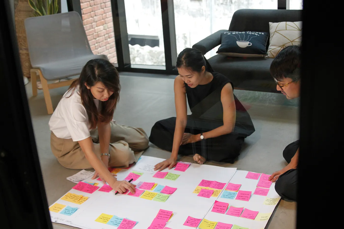 Three people sitting on the floor around a large piece of paper with sticky notes on it