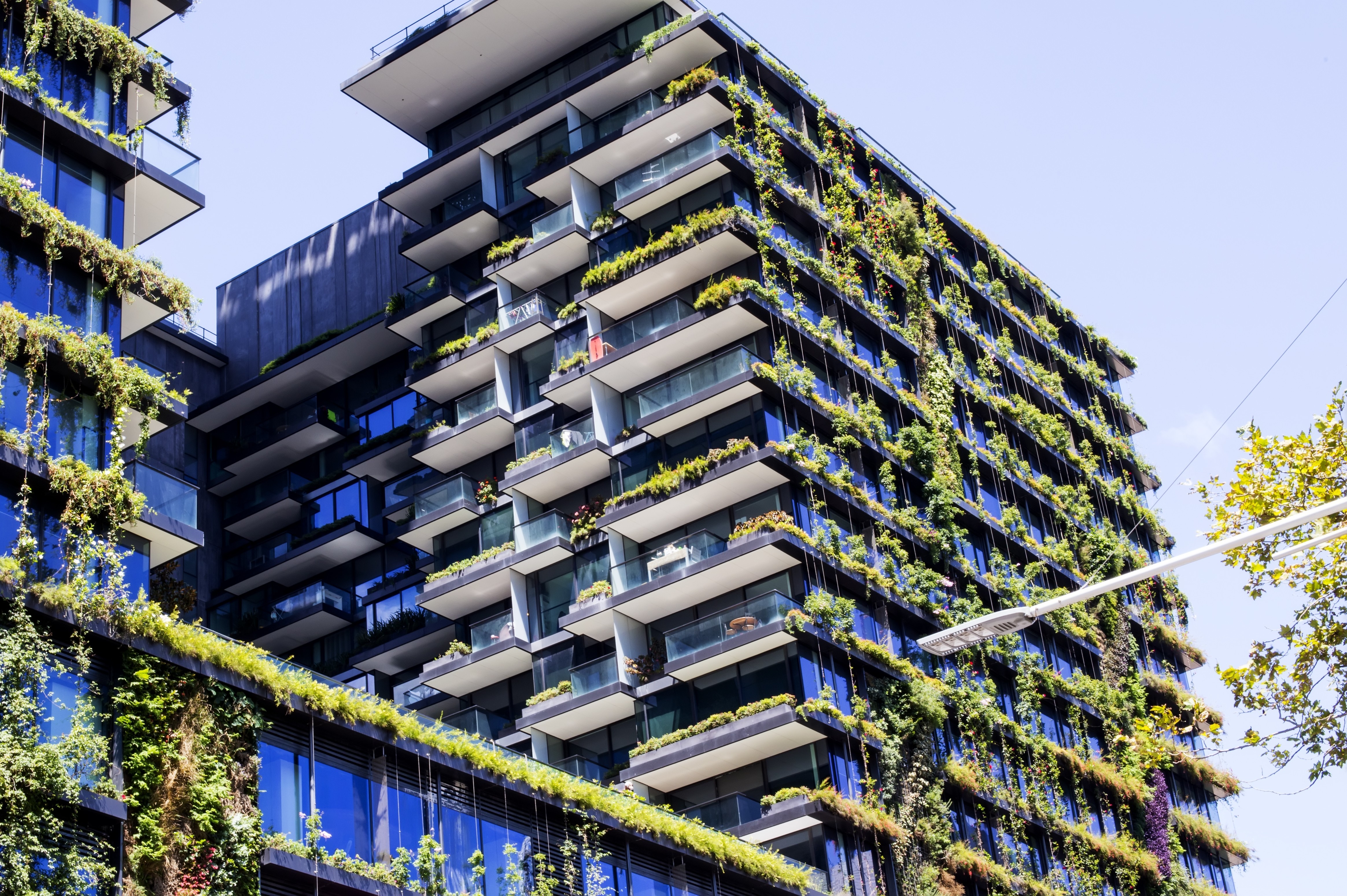 A man stands while two people sit at a table in an office setting, smiling and engaged in conversation. The mood is friendly and collaborative.