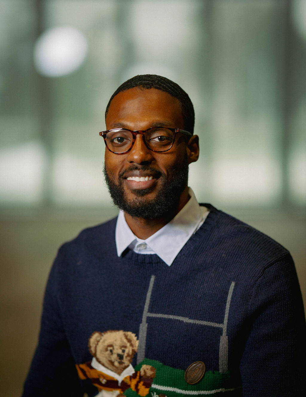 A man in a gray blazer and brown vest, with gray-streaked hair, poses against a neutral background.