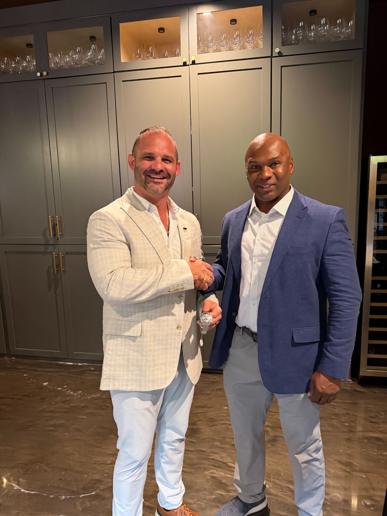 Anthony Boyd shakes hands with a man in a blue blazer while holding a watch indoors.