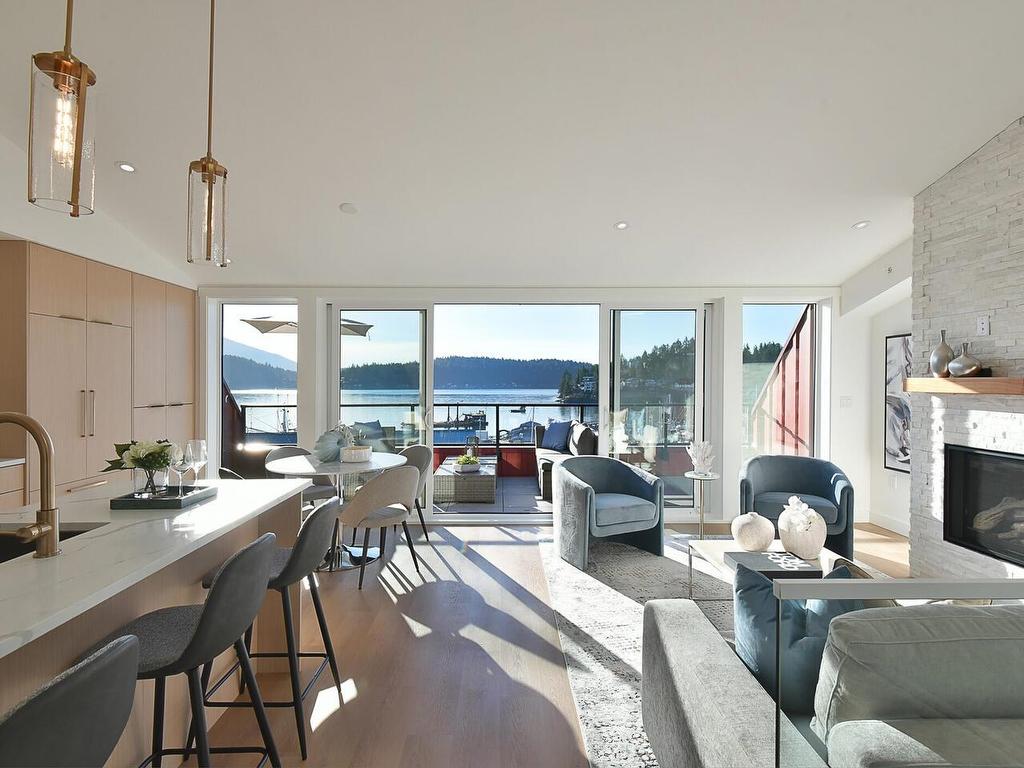 Modern open-concept living space with views of water, featuring a kitchen, seating area, and large windows.