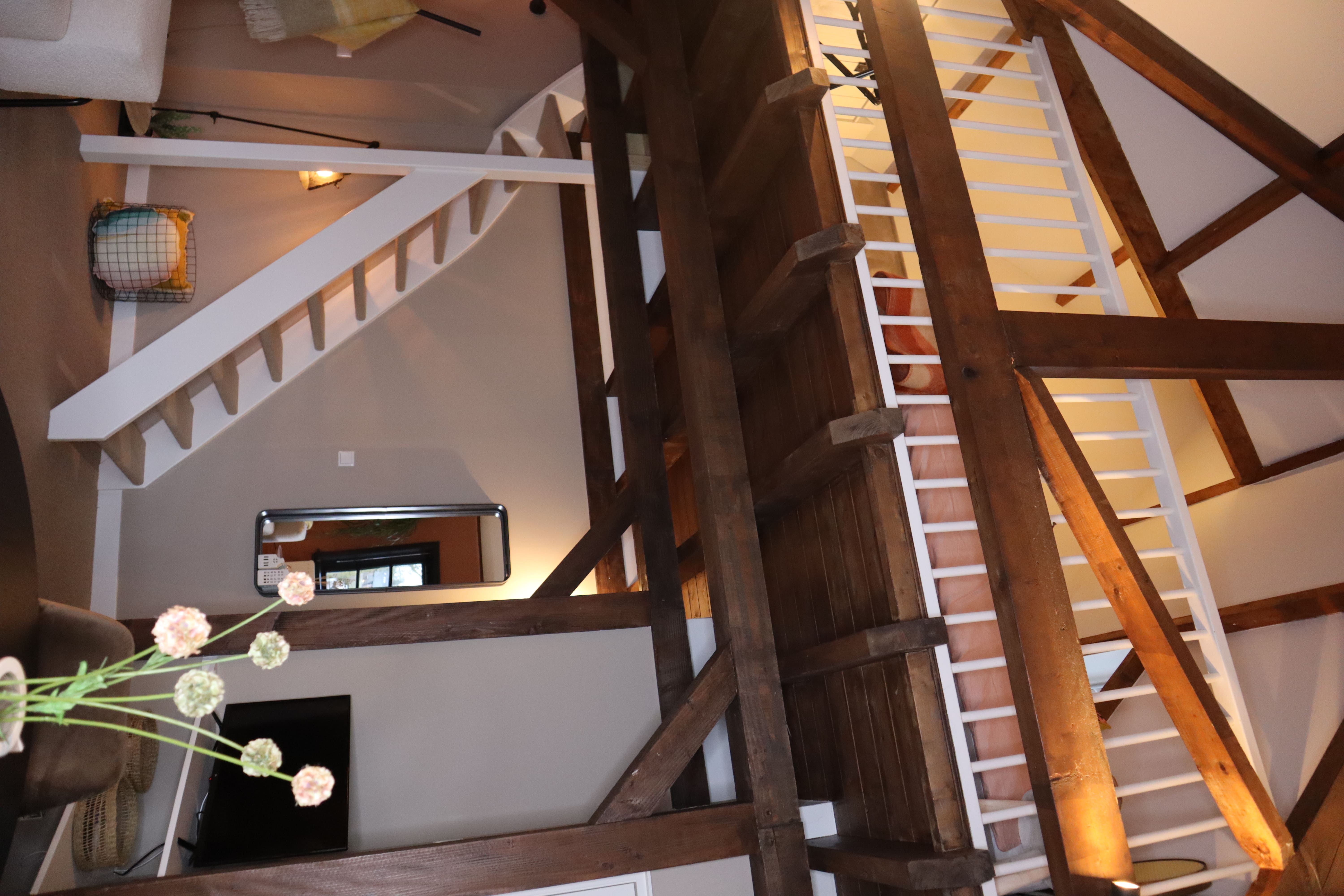 Uitzicht vanuit de bovenverdieping op de woonkamer, met houten balken en een trap.