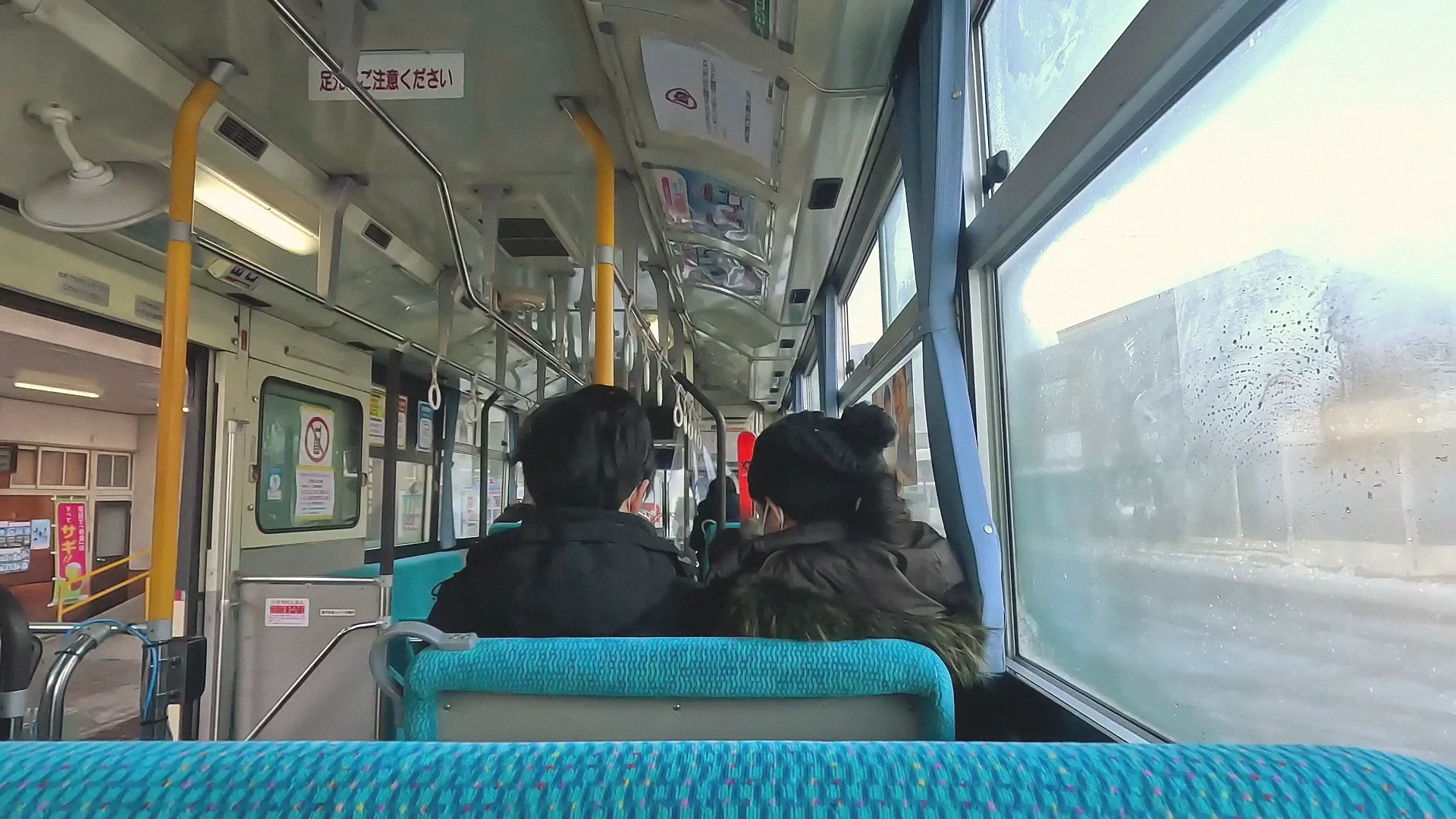 Inside a local Nagaden bus in winter, passengers seated, snow and a fogged window outside.