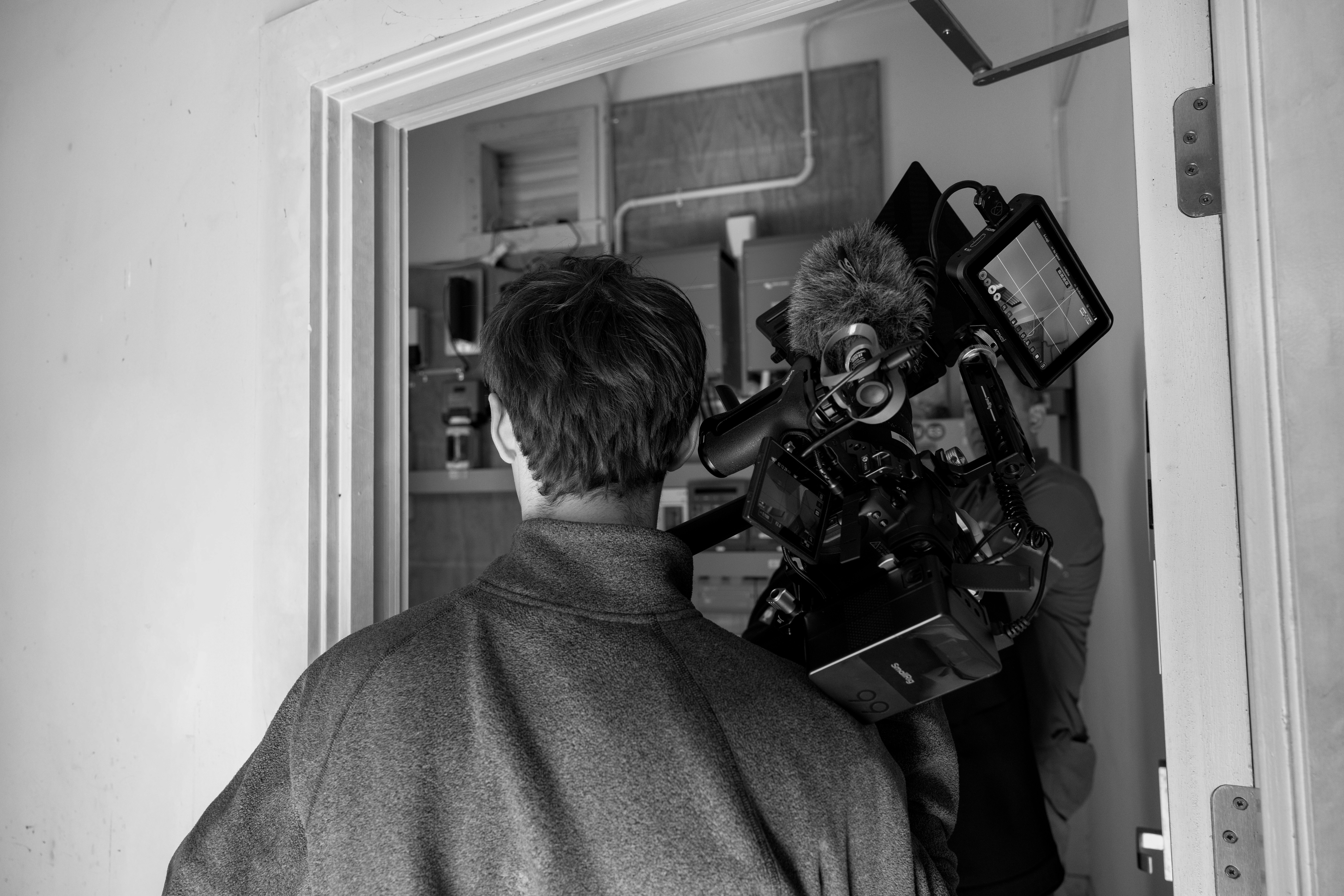 Modern red brick apartment or office building viewed from below against a blue sky, showcasing its geometric architecture with evenly spaced windows and balconies.
