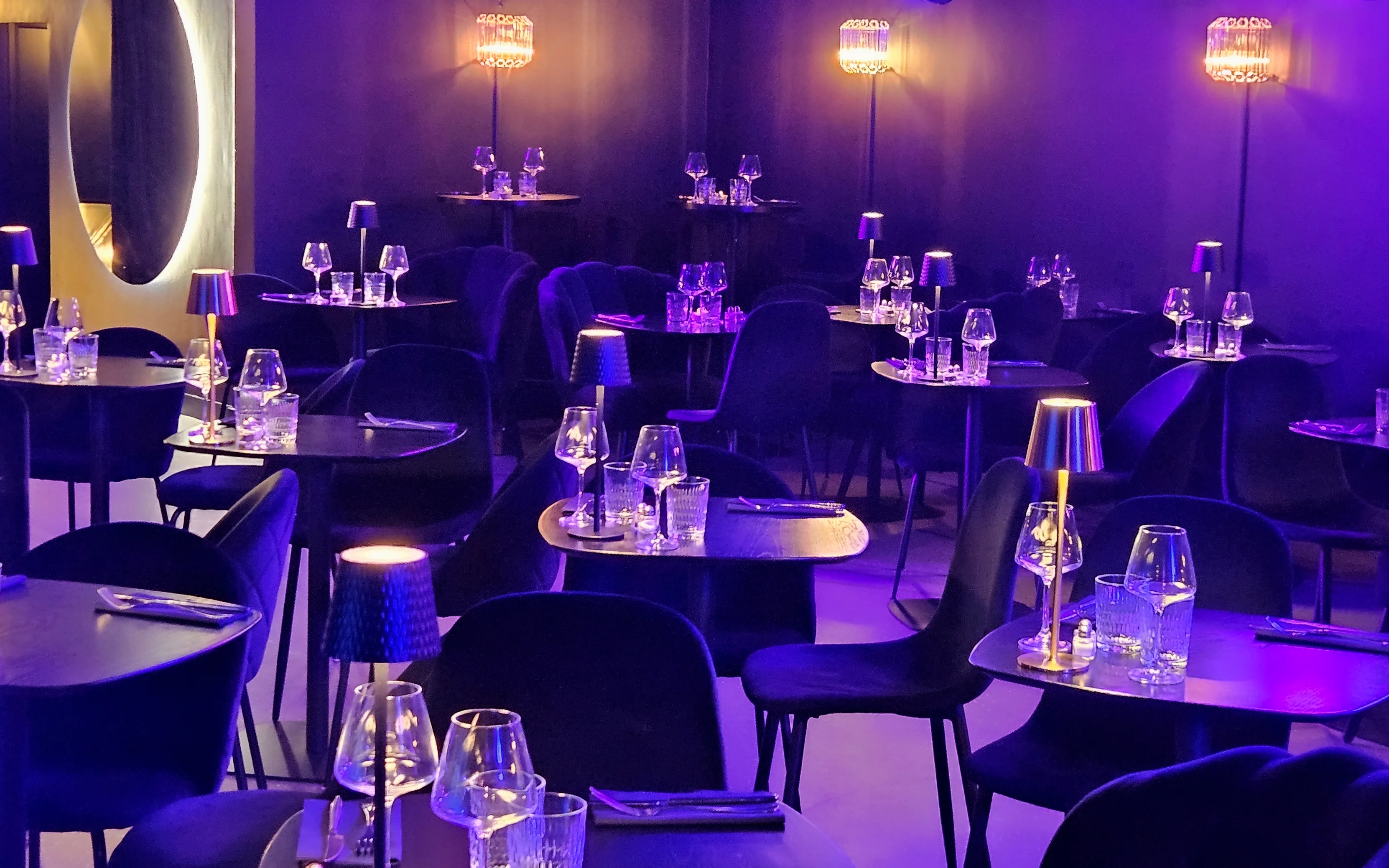 Dark and intimate photograph of a dedicated dining section within the cabaret, featuring multiple tables precisely set with small lamps and warm spotlights, ready for a group reservation.