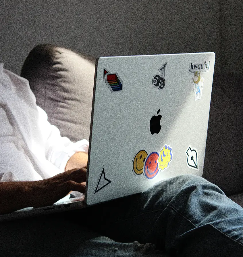 Karim working on a laptop decorated with colorful stickers while relaxing.