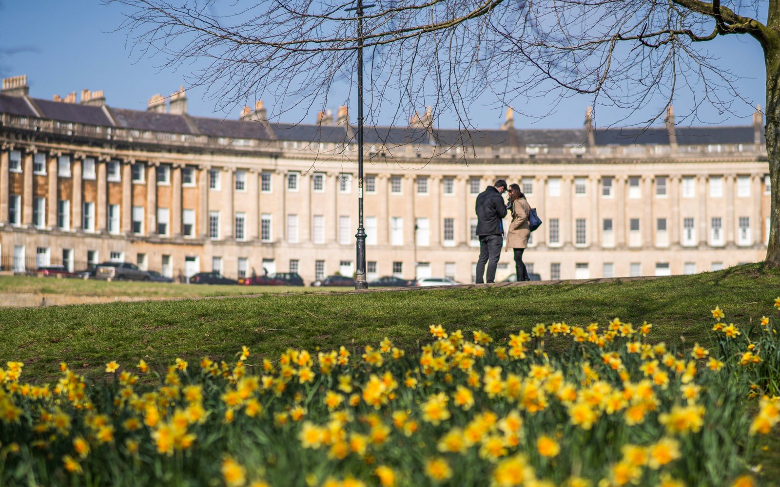 Royal Crescent in Bath with visitors on Bridgerton tour, daffodils in foreground.